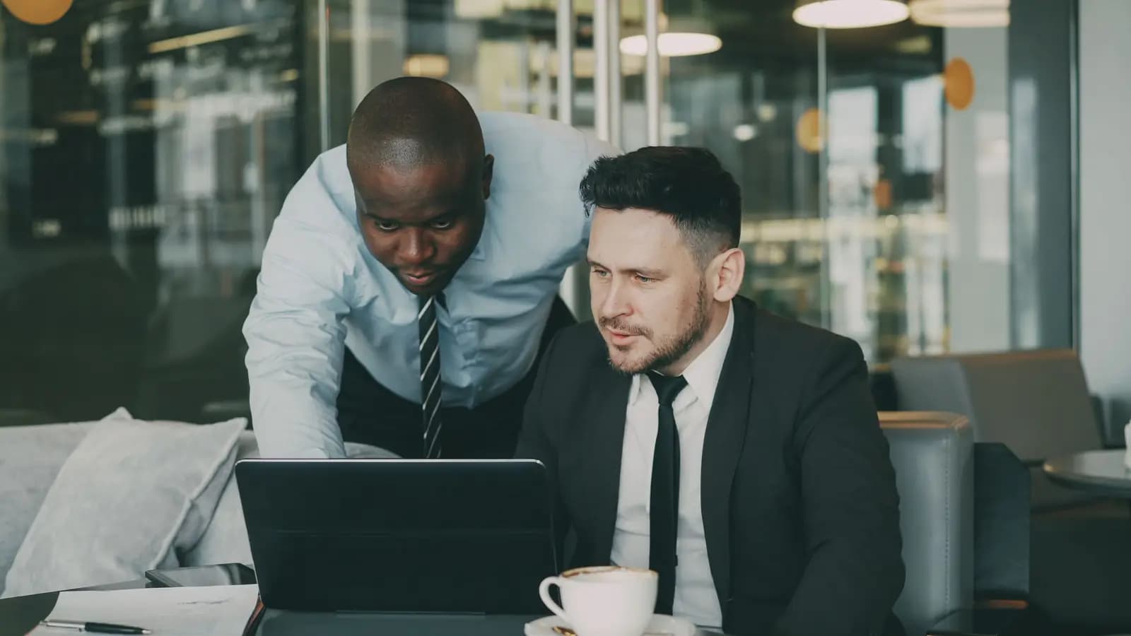 Zwei Kollegen besprechen in einem modernen Büro gemeinsam einen Arbeitsstand am Laptop.
